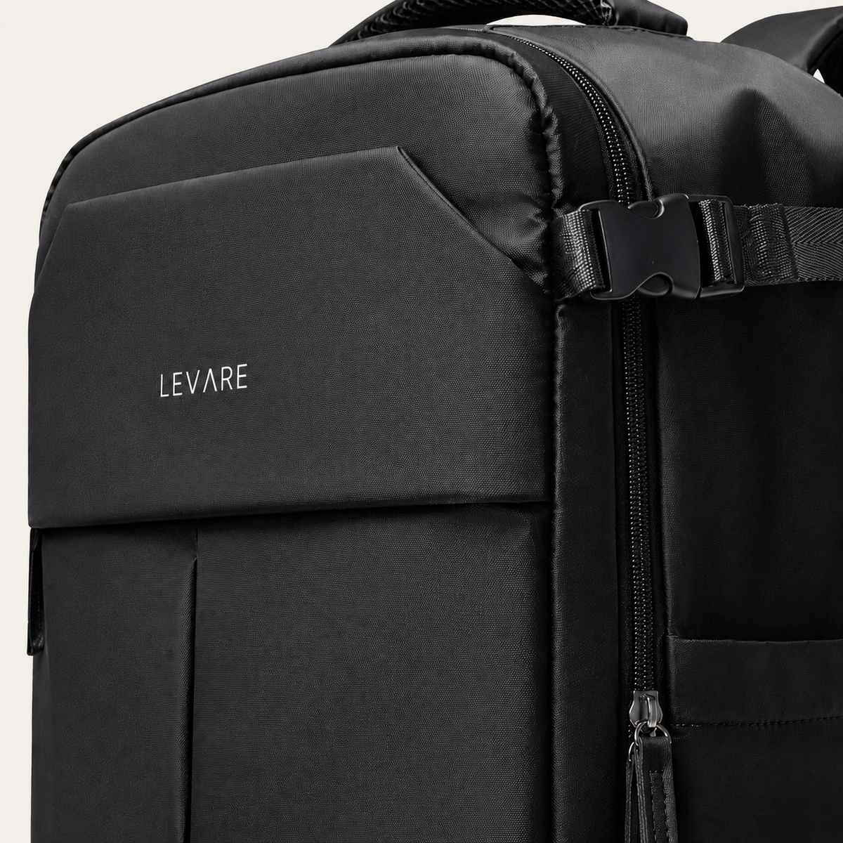 Close-up of a black LEVARE travel backpack showing the front pocket with silver brand lettering, a side zipper with black plastic buckle, and a pocket on the right side.